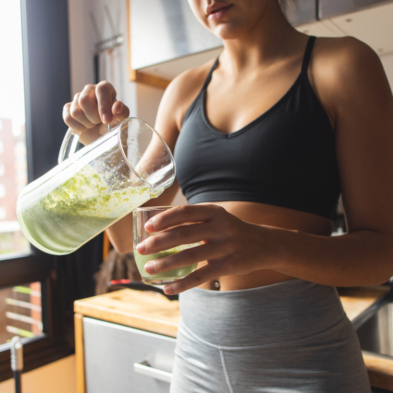 Frau in Sportkleidung schenkt sich grünen Detox-Smoothie ein