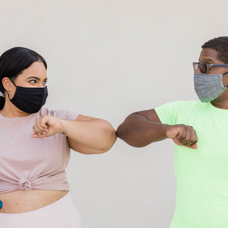 Zwei Menschen mit Op-Masken, die sich per Ellenbogen-Check begrüßen