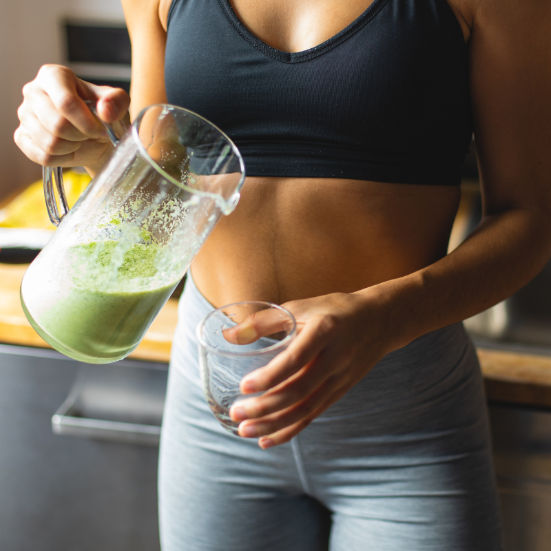 Frau in Sportkleidung schenkt sich grünen Detox-Smoothie ein